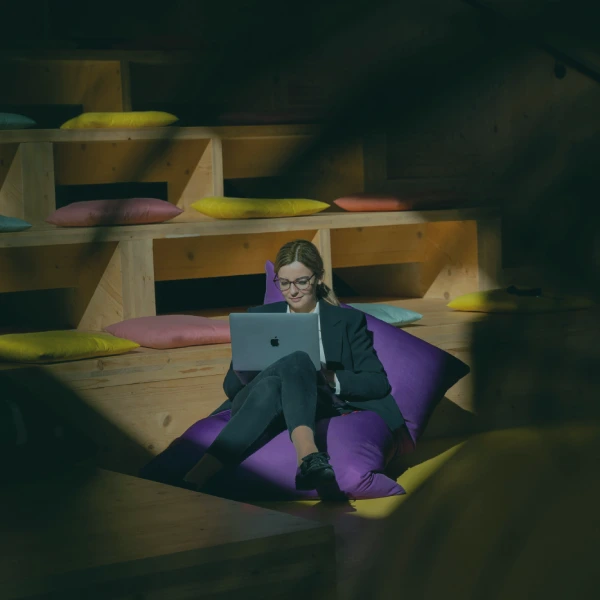 A person working on a laptop, seated on a large purple beanbag in a wooden loft