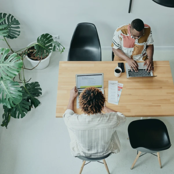 Two people working on laptops at a shared wooden table